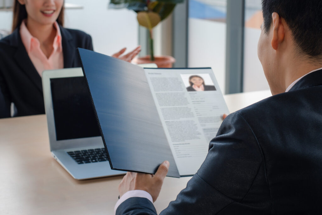 A hiring manager reviewing a job applicant’s resume while interviewing her.